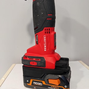 May include: A red and black Craftsman cordless drill with a black and orange Ridgid Hyper Lithium Ion battery attached.