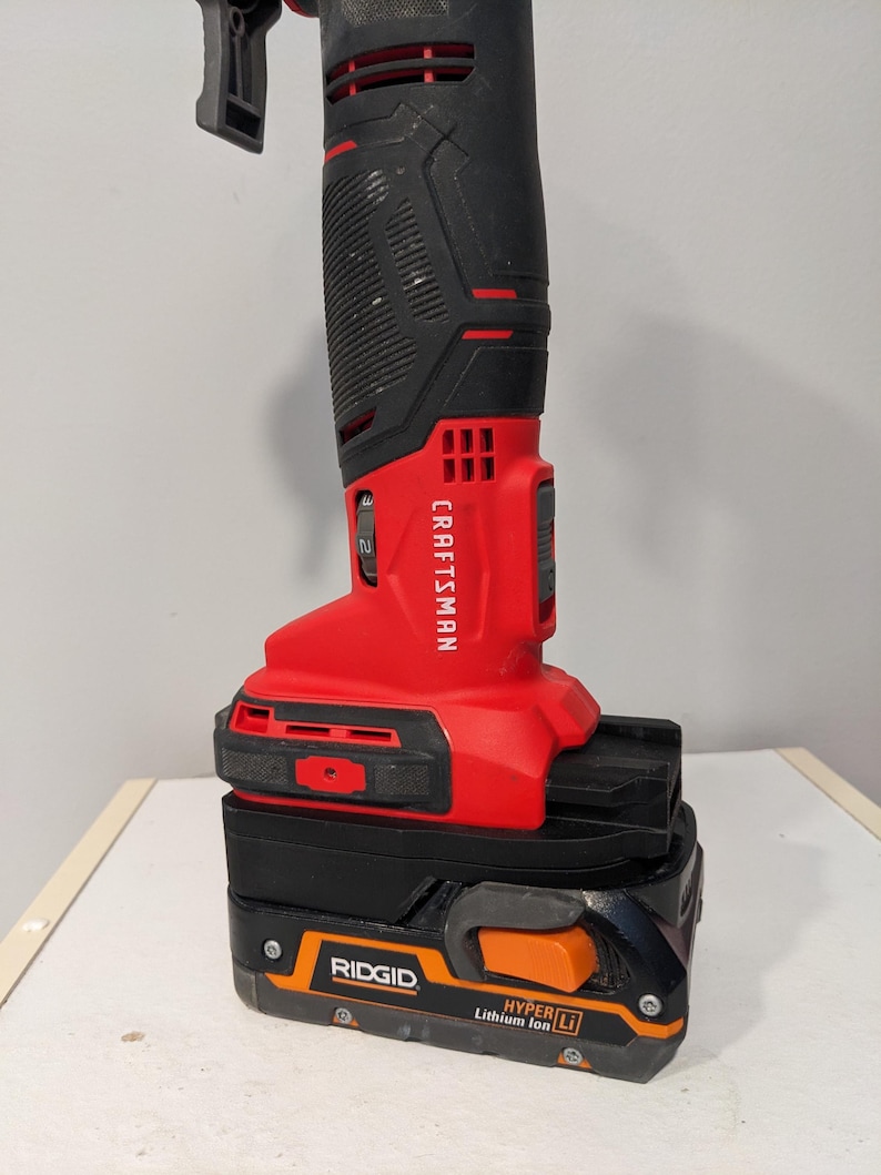 May include: A red and black Craftsman cordless drill with a black and orange Ridgid Hyper Lithium Ion battery attached.