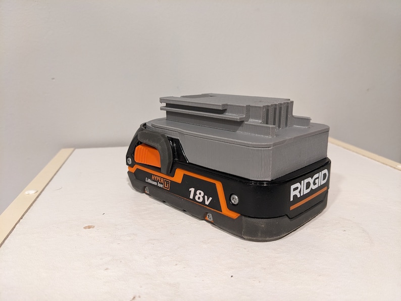 Pu&ograve; includere: Una batteria Ridgid 18V Hyper Lithium-Ion grigia e nera con un pulsante di rilascio arancione.