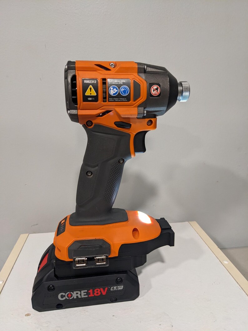Op de afbeelding: Een oranje en zwarte draadloze schroevendraaier met een CORE18V 4.0 batterij. De schroevendraaier heeft een ingebouwde LED-lamp en een riemclip.