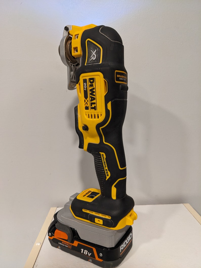 May include: A yellow and black DeWalt XR 20V cordless oscillating tool with a brushless motor. The tool is attached to a Ridgid 18V lithium-ion battery.