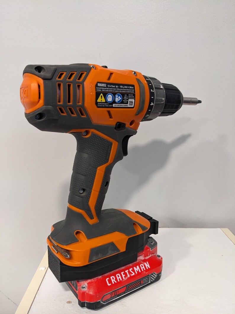 May include: An orange and black cordless drill with a red 20V Craftsman battery attached. The drill has a black handle and a silver drill bit. The drill has a speed setting dial and a trigger.