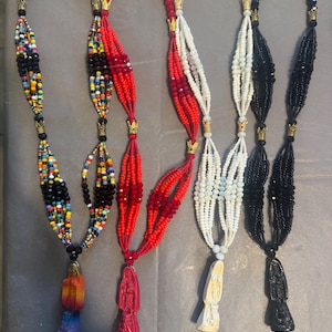 Puede incluir: Cuatro collares de cuentas con cuentas de diferentes colores y figuras religiosas como colgantes. Los collares son rojo, blanco, negro y multicolor.