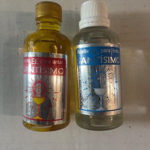 Könnte beinhalten: Zwei transparente Glasflaschen mit Flüssigkeit. Eine hat einen goldenen Deckel und gelbe Flüssigkeit, die andere einen weißen Deckel und klare Flüssigkeit. Beide haben silberne Etiketten mit Text und religiösen Bildern.