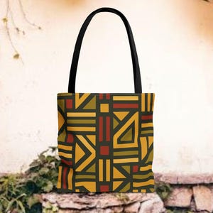 May include: A tote bag with a black handle and a geometric pattern in shades of yellow, red, and green on a dark background. The bag is made of a sturdy material and is designed for carrying items.