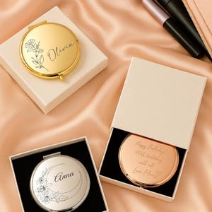 May include: Gold and silver compact mirrors with floral designs and personalised text. One mirror is gold with the name "Olivia", another is silver with "Anna", and a third is rose gold with a birthday message.