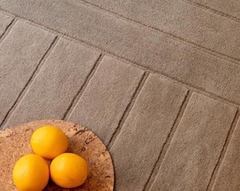 Puede incluir: Primer plano de una alfombra texturizada de color topo con un patrón geométrico. Tres limones amarillos brillantes descansan sobre una tabla redonda de corcho. El diseño de la alfombra presenta secciones rectangulares elevadas.