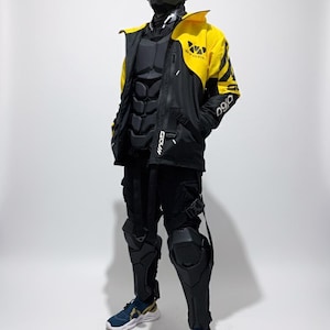 May include: A futuristic black and yellow outfit, including a jacket, pants, and protective gear. The jacket has yellow accents and the number "090" printed on the sleeve. The outfit is paired with a black face mask and blue sneakers.