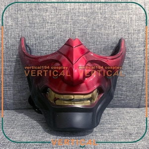 May include: A red and black Oni mask with a menacing grin and sharp teeth. The mask has a textured surface and is designed with sharp angles and curves. The text "vertical194 cosplay" is printed on the mask.
