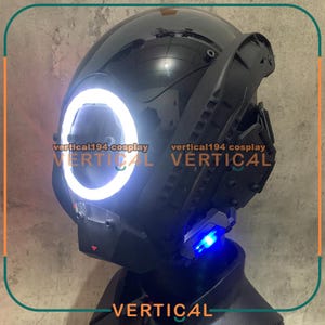 May include: A black helmet with a white ring around the front. The helmet has a blue light on the side. The text "vertical194 cosplay VERTICAL" is visible on the helmet.