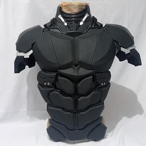 Puede incluir: Una pieza de armadura de torso negra que presenta una placa de pecho segmentada, placas abdominales y hombreras. El diseño incluye detalles de color plateado en el cuello y las articulaciones de los hombros, con remaches metálicos visibles.