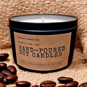 Puede incluir: Un tarro de vela de metal negro con una etiqueta de papel marrón que dice "Carlile Candle Co. Morning Java - 8oz Hand-Poured Soy Candles https://carlilecandleco.etsy.com". La vela está rodeada de granos de café.