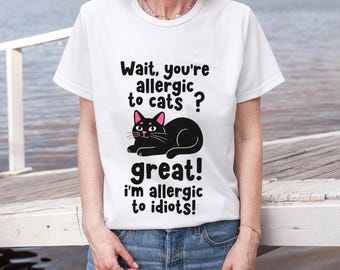 Puede incluir: Camiseta blanca con un gato negro y el texto: "¿Espera, eres alérgico a los gatos? ¡Genial! ¡Soy alérgico a los idiotas!" El gato tiene orejas y nariz rosas.