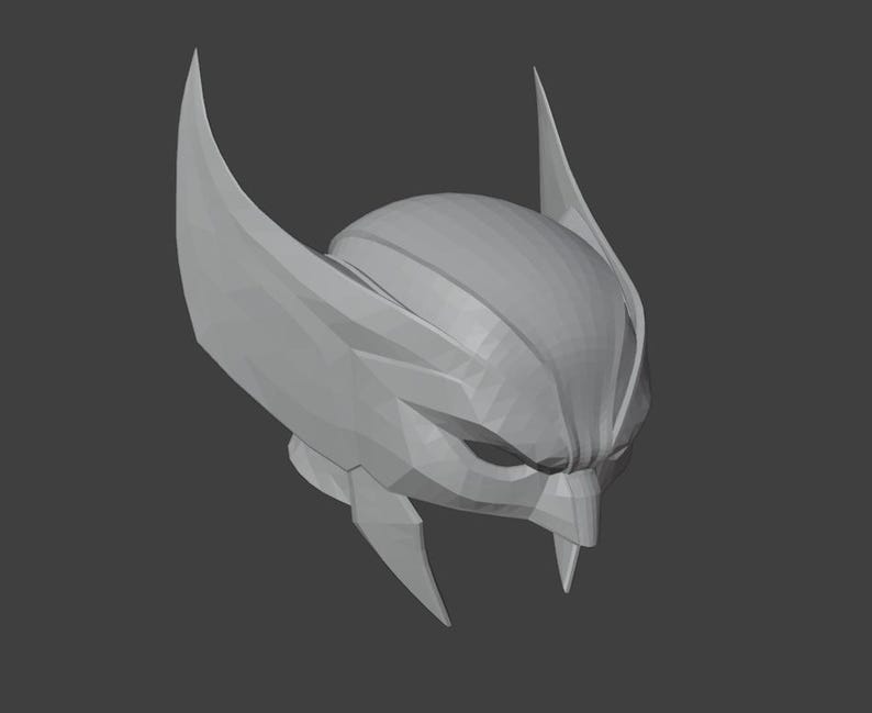 K&ouml;nnte beinhalten: Ein graues 3D-gedrucktes Modell eines Helms mit einem spitzen, kantigen Design. Der Helm hat zwei gro&szlig;e, spitze Ohren an den Seiten und einen spitzen Kinnschutz.