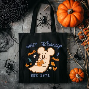 May include: Black tote bag with a Halloween-themed Walt Disney design. The design features a ghost-like Mickey Mouse holding a pumpkin-shaped candy bucket, surrounded by autumn leaves and skulls. The text "WALT DISNEY EST. 1971" is printed on the bag.