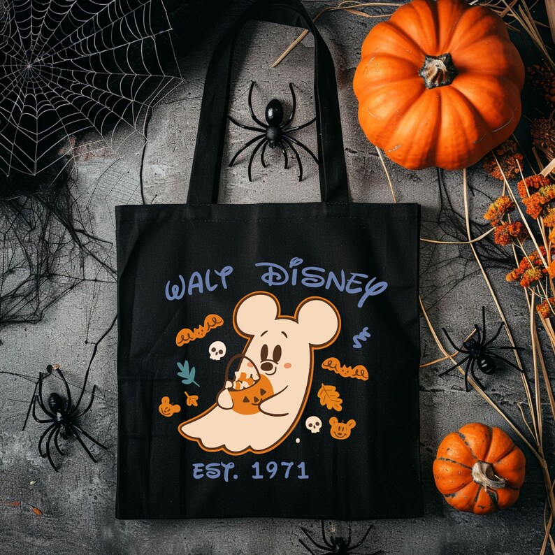 May include: Black tote bag with a Halloween-themed Walt Disney design. The design features a ghost-like Mickey Mouse holding a pumpkin-shaped candy bucket, surrounded by autumn leaves and skulls. The text "WALT DISNEY EST. 1971" is printed on the bag.