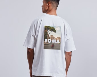 Könnte beinhalten: Weißes T-Shirt mit einem Grafikdruck einer Stadtlandschaft mit dem Wort "ROMA" in weißen Buchstaben. Die Grafik ist mittig auf der Rückseite des Shirts platziert.