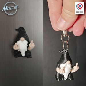 Peut inclure: Figurine de gnome noir avec une barbe blanche et un majeur levé. Le gnome porte un chapeau et une chemise noirs. Un gnome similaire est fixé à un aimant. L'image montre également une version porte-clés du gnome.