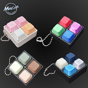 May include: A collection of keycap-shaped accessories in various colors, including pink, orange, white, red, green, purple, blue, navy, light green, brown, and beige. Each set of four keycaps is held in a square tray and attached to a silver chain.