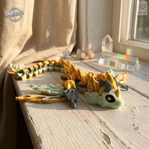 Puede incluir: Una detallada figura de dragón articulada en tonos dorados, verdes y grises, sobre una superficie de madera blanca. El dragón tiene detalles intrincados, incluyendo escamas y alas. Fabricado en Francia.