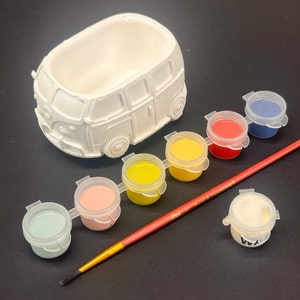 May include: A white ceramic Volkswagen bus planter with six small paint pots and a paintbrush. The paint pots are yellow, red, blue, light blue, pink, and white.
