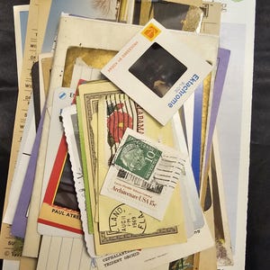 Puede incluir: Una colección de efímeras vintage, que incluye postales, sellos y una diapositiva Kodak Ektachrome. Los artículos están superpuestos, con una variedad de colores y texturas. Algunos artículos tienen texto, incluyendo "Lovely cut flowers" y "Architecture USA 15c".
