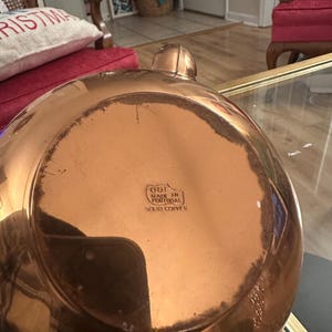 Peut inclure: Une bouilloire en cuivre avec une finition brillante. Le fond de la bouilloire porte une &eacute;tiquette indiquant "ODI Fabriqu&eacute; au Portugal Cuivre massif."