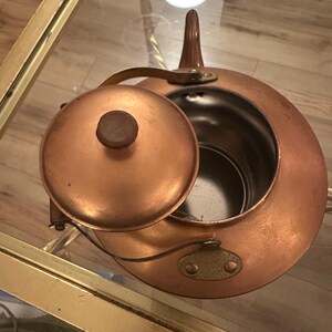 Peut inclure: Une th&eacute;i&egrave;re en cuivre avec un couvercle et une poign&eacute;e. La th&eacute;i&egrave;re est sur une table en verre avec une bordure dor&eacute;e.