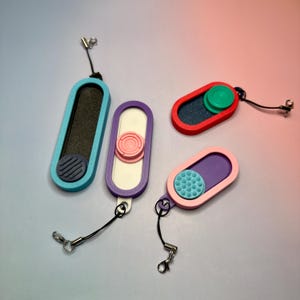 Può includere: Quattro portachiavi rettangolari colorati con un piccolo design circolare su ciascuno. I portachiavi sono in tonalità di blu, viola, rosso e rosa, con cordini neri e chiusure argentate. Design moderno e minimalista.