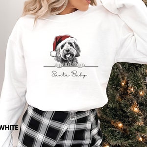 May include: White sweatshirt with a graphic of a dog wearing a Santa hat. The dog is peeking over a line with the text "Santa Baby" in a script font. The word "WHITE" is printed in a bold font at the bottom left.