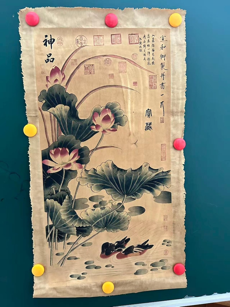 May include: An antique-style artwork featuring a lotus pond scene with ducks, lotus flowers, and large leaves. The artwork has Chinese characters and is attached to a green surface with yellow and pink magnets.
