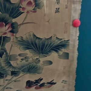 May include: An antique Asian-style painting featuring lotus flowers, lily pads, and ducks. The artwork is primarily in shades of green, pink, and brown, with some visible text in the upper right corner. The painting is held in place with red and yellow push pins.
