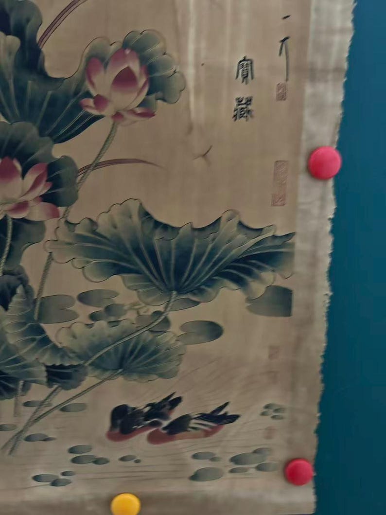 May include: An antique Asian-style painting featuring lotus flowers, lily pads, and ducks. The artwork is primarily in shades of green, pink, and brown, with some visible text in the upper right corner. The painting is held in place with red and yellow push pins.