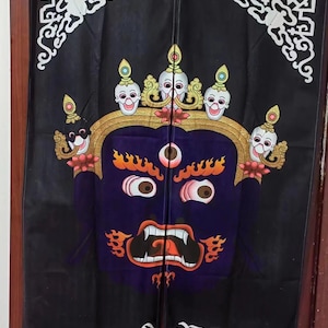 May include: Black fabric door curtain featuring a stylized, colorful illustration of a deity with a fierce expression. The design includes a purple face, orange flames, and white skull-like figures. White decorative patterns are at the top.