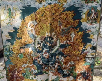 May include: A colorful Tibetan Buddhist thangka painting depicting a deity with multiple arms and heads, surrounded by other figures and symbols. The deity is blue and gold, with a fierce expression. The painting is set against a dark blue background with clouds and flames.