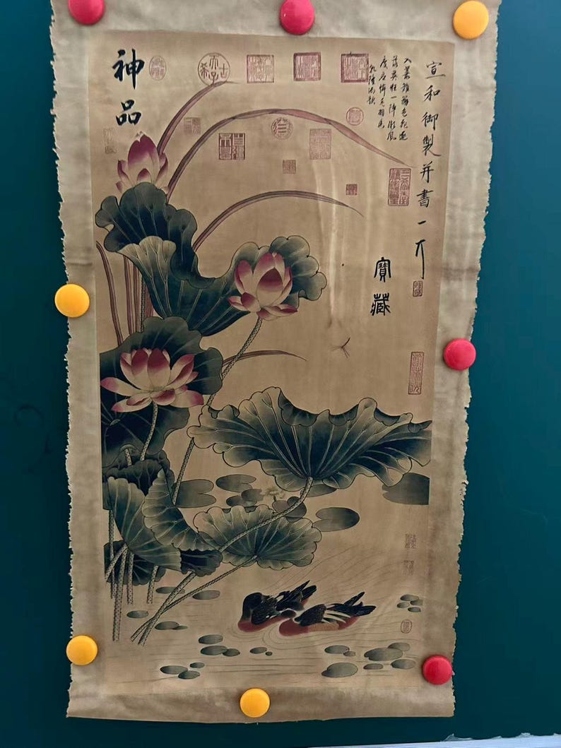 May include: A vintage scroll painting featuring a detailed depiction of lotus flowers and leaves in a pond, with two ducks swimming. The artwork includes Chinese calligraphy and seals, and is held in place by colorful magnets.
