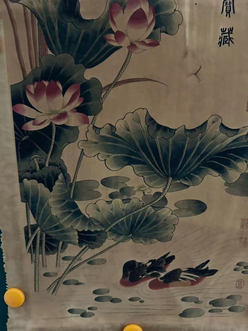 May include: An Asian-style painting featuring lotus flowers with pink and white petals, large green leaves, and two ducks swimming in a pond. The artwork has a muted color palette with a beige background and traditional calligraphy.