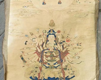 Op de afbeelding: Een vintage scrollschildering die een meerarmige godheid afbeeldt die op een lotusthron zit. De godheid heeft een serene uitdrukking en is omringd door wolken en vliegende vogels. Het schilderij is gemaakt in tinten goud, rood, blauw en groen.