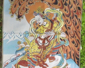 May include: A tapestry depicting a seated figure in elaborate yellow and red robes, set against a backdrop of a stylized tree and mountains. The artwork has a detailed, colourful design with a spiritual theme.