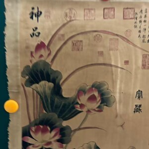 May include: An antique scroll painting featuring lotus flowers and leaves in shades of pink, green, and white. The artwork includes Chinese characters and seals, with the scroll held in place by pink and yellow magnets.
