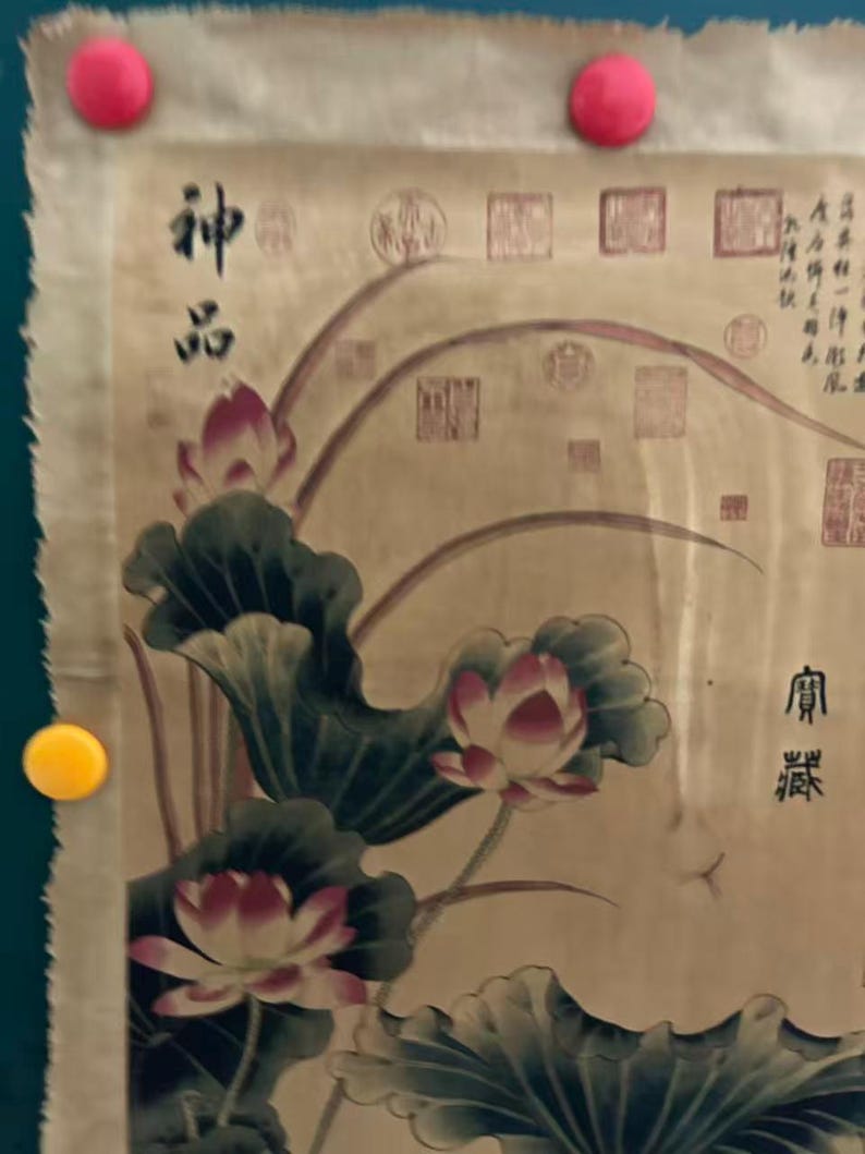 May include: An antique scroll painting featuring lotus flowers and leaves in shades of pink, green, and white. The artwork includes Chinese characters and seals, with the scroll held in place by pink and yellow magnets.