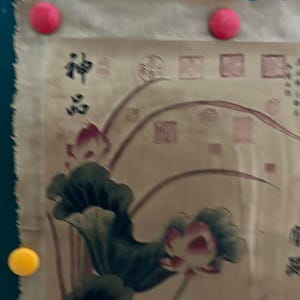 May include: A beige scroll with a floral design featuring lotus flowers and leaves in pink and green. The scroll is held in place by three round magnets, two pink and one yellow. The text "神品" is visible.