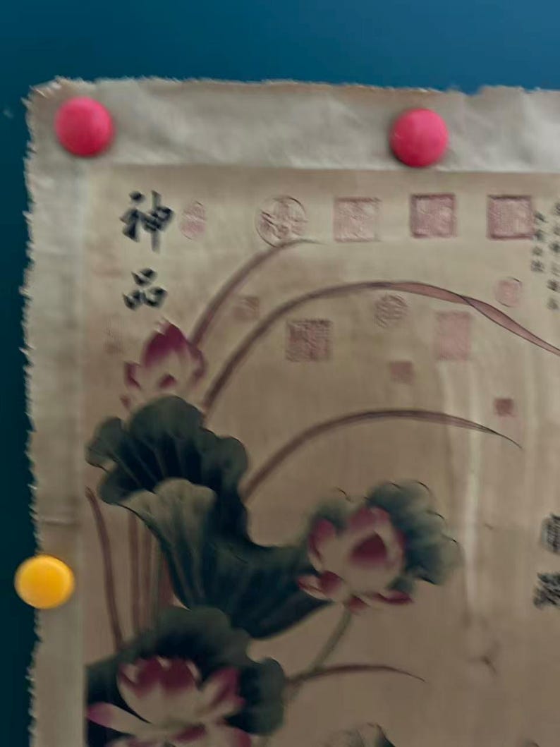 May include: A beige scroll with a floral design featuring lotus flowers and leaves in pink and green. The scroll is held in place by three round magnets, two pink and one yellow. The text "神品" is visible.