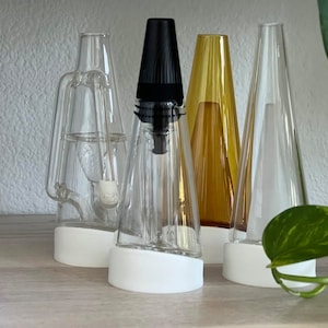 May include: Four glass water pipes with white bases. The pipes are clear glass, amber glass, and two clear glass pipes with different designs. The pipes are arranged in a row on a wooden surface.