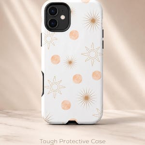 May include: White phone case with a repeating pattern of gold suns and peach-colored circles. The case has a black camera cutout and the words "Tough Protective Case" printed on the bottom.