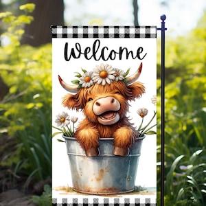 May include: A welcome garden flag with a black and white checkered border. A cartoon Highland cow with a daisy flower crown is sitting in a metal bucket. The cow is smiling and has a brown and white coat.