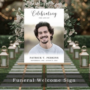 May include: A white sign with black text announcing a funeral for Patrick T. Perkins. The sign reads "Celebrating the Life of Patrick T. Perkins, September 9, 1982 - August 21, 2024". The sign is on a wooden easel and is in front of a pathway lined with lanterns.