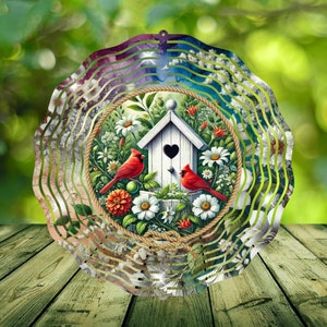 May include: Metal wind spinner with a circular design featuring a birdhouse with two red cardinals, flowers, and leaves. The background is a swirling pattern of blue, green, and white.
