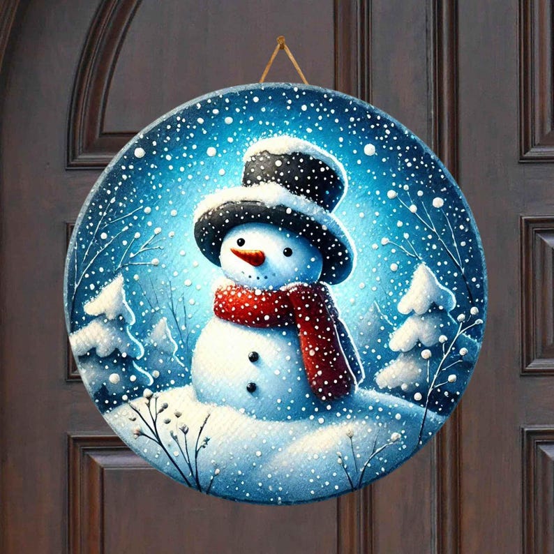 May include: A round, blue and white winter scene door hanger with a snowman wearing a black hat and red scarf. The snowman is standing in a snowy landscape with pine trees and falling snow.