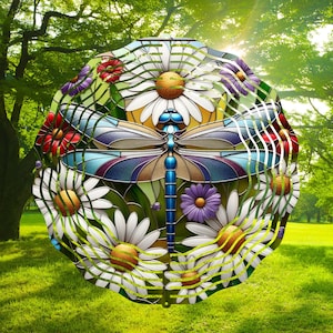 Puede incluir: Un móvil de vidrio coloreado que presenta una libélula con alas azules y un cuerpo con detalles en morado, marrón y amarillo. La libélula está rodeada de margaritas blancas con centros amarillos.
